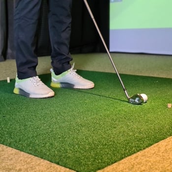 Basement golf simulator setup with screen, turf, and swing space