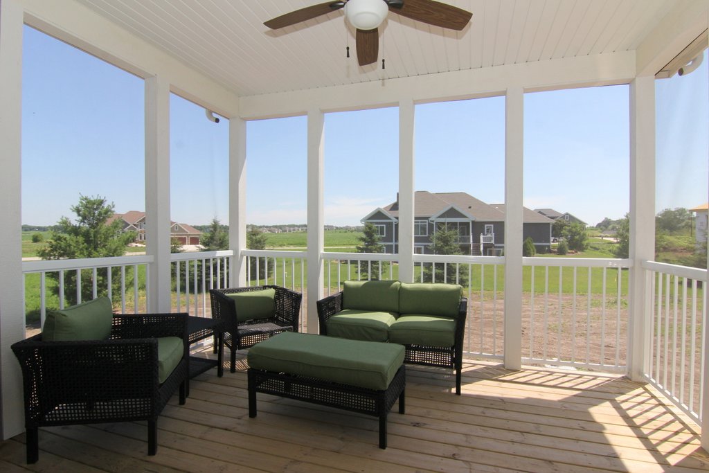A screened in porch with wooden floors and green outdoor furniture overlooking a backyard.