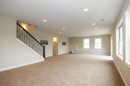 A finished, brightly lit open concept basement with a staircase and windows.